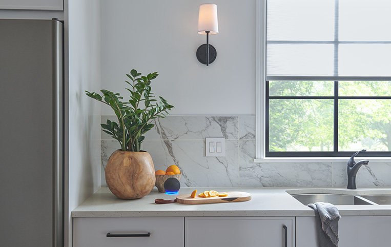 Lighting controls on a marble backsplash in a minimalist kitchen showcasing integraion with an Amazon Echo Dot.