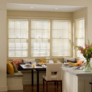 Windows with wood blinds surrounding a dining banquette.